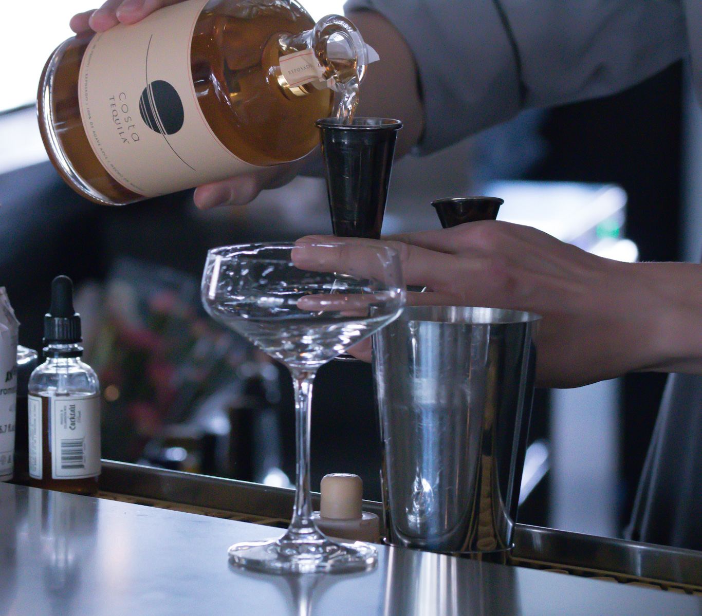 Johnny measuring a pour with a jigger into a coupe glass behind the bar