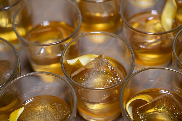 Rows of old fashioneds with orange twists on large ice